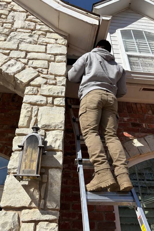 Technician on a ladder inspecting a home's eaves and soffit